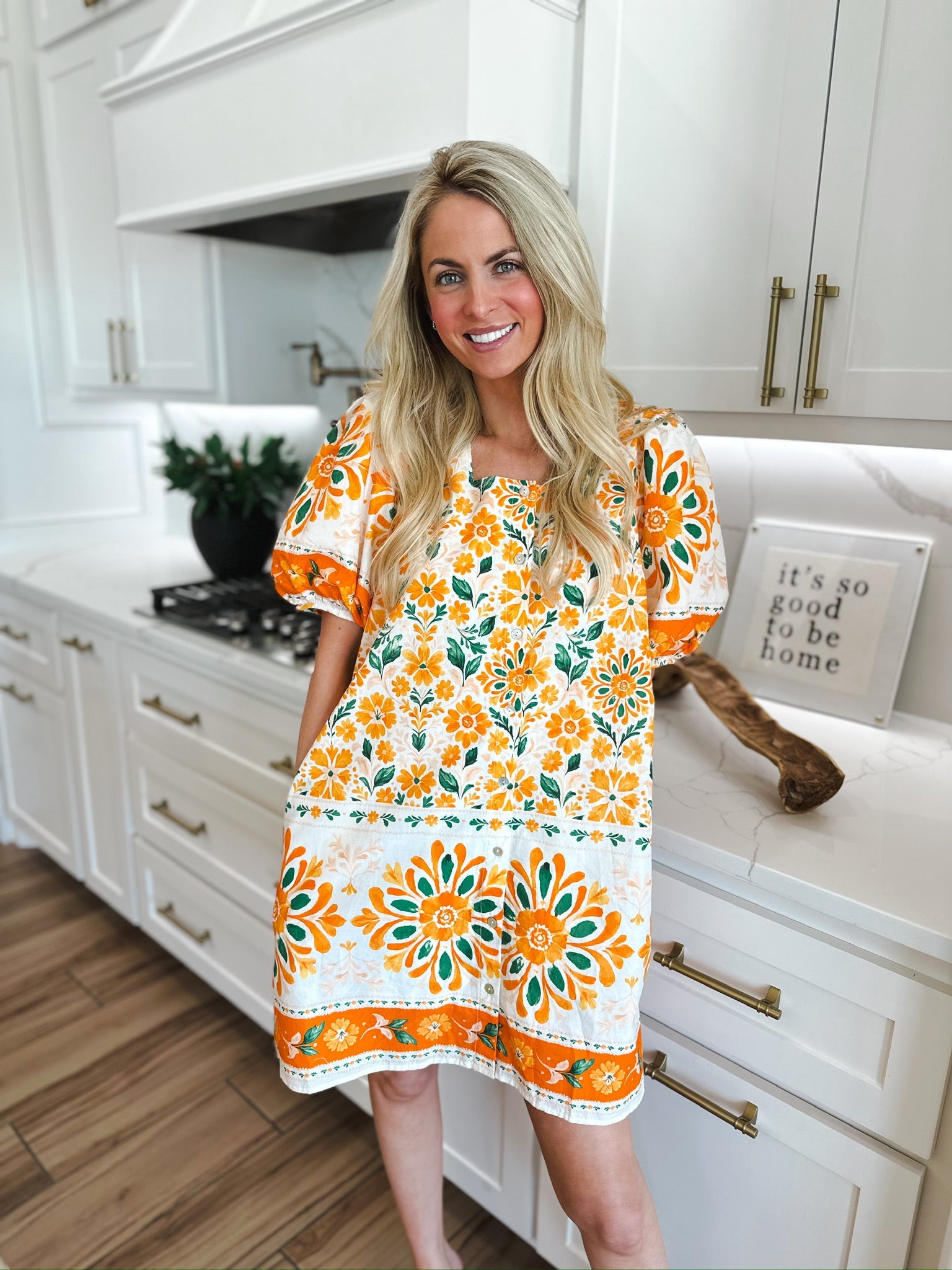 Woman in an Entro orange floral puff sleeve mini dress with white and green floral patterns, standing in a modern kitchen.