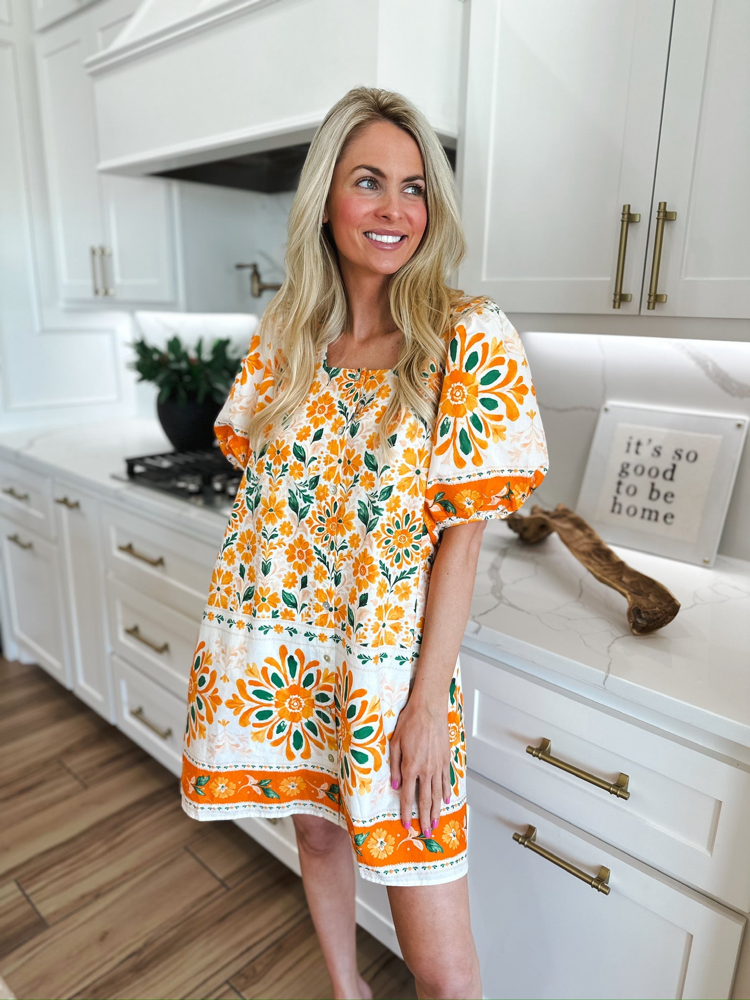 Woman in a white mini dress with an orange floral print and puff sleeves. Features a square neckline and a banded hem with