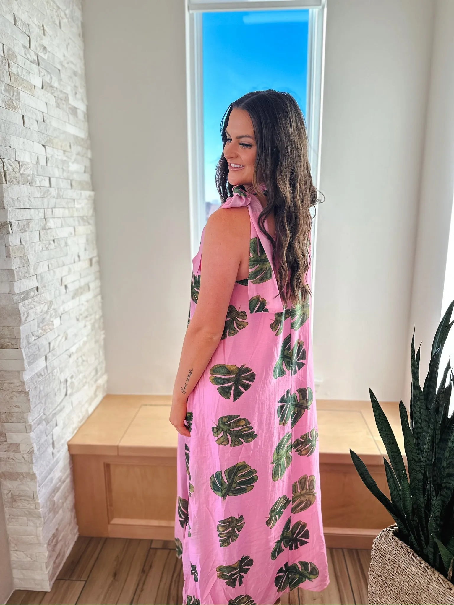 Entro pink maxi dress with green palm leaf print and tie neck. Woman wearing the dress from the back.