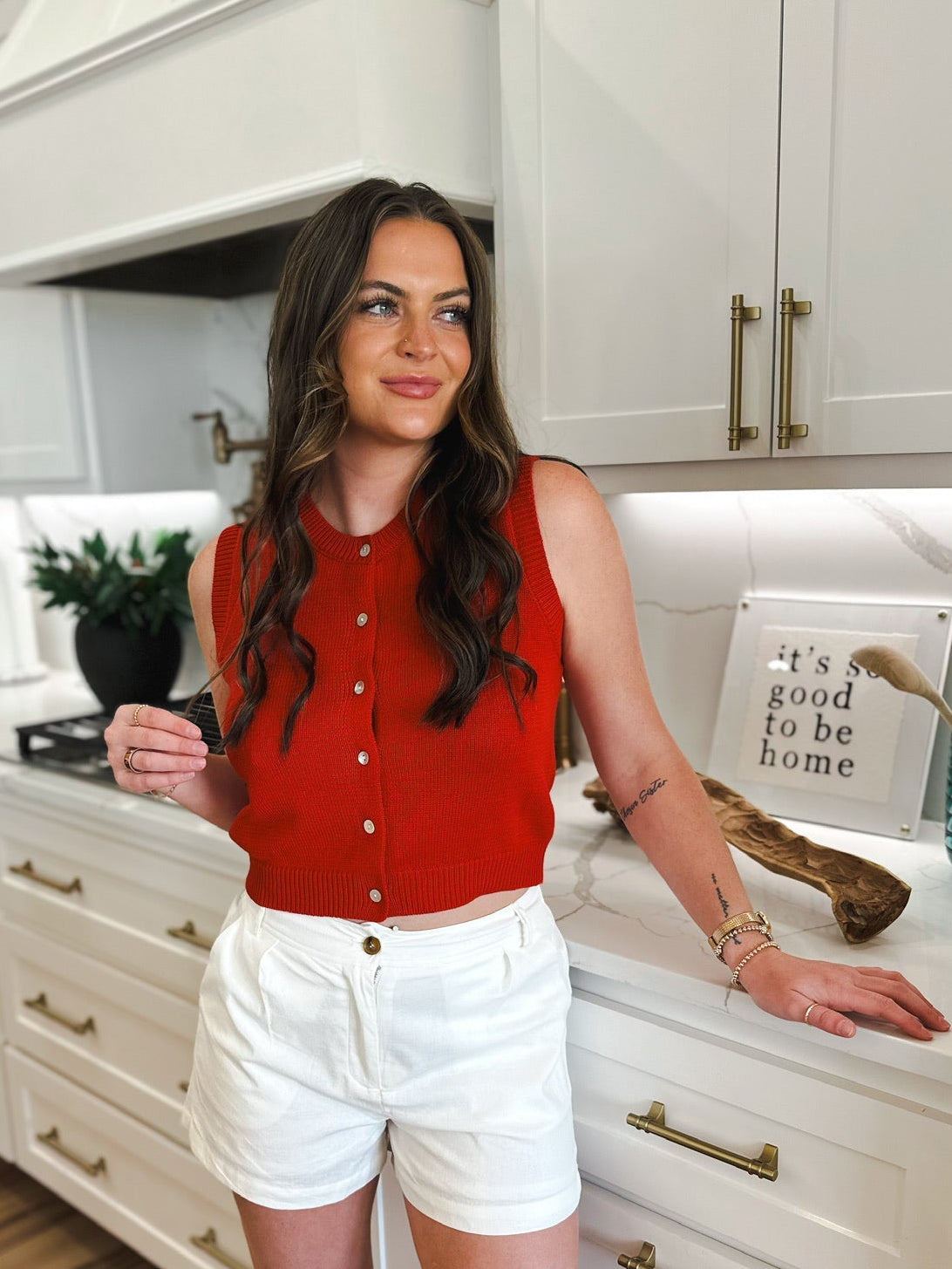 Woman in red sleeveless scoopneck button-down tank top and white shorts standing in a kitchen.