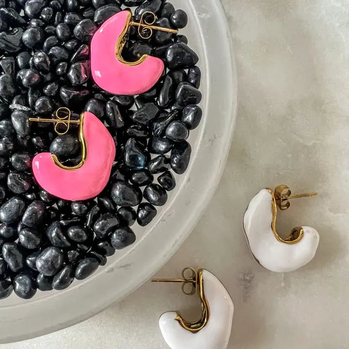 Erma pink enamel 18K gold plated waterproof huggie earrings and white enamel earrings with gold trim, displayed on black