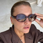 Freyrs Aria womens classic oval acetate sunglasses in deep brown with gradient lenses reflecting palm trees. Woman adjusts