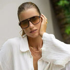 Freyrs Billie unisex aviator sunglasses with black frames and gradient brown lenses, worn by a woman with golden hoop
