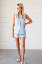 Woman wearing a baby blue gingham romper with a sleeveless vest and shorts. The romper features button details and a
