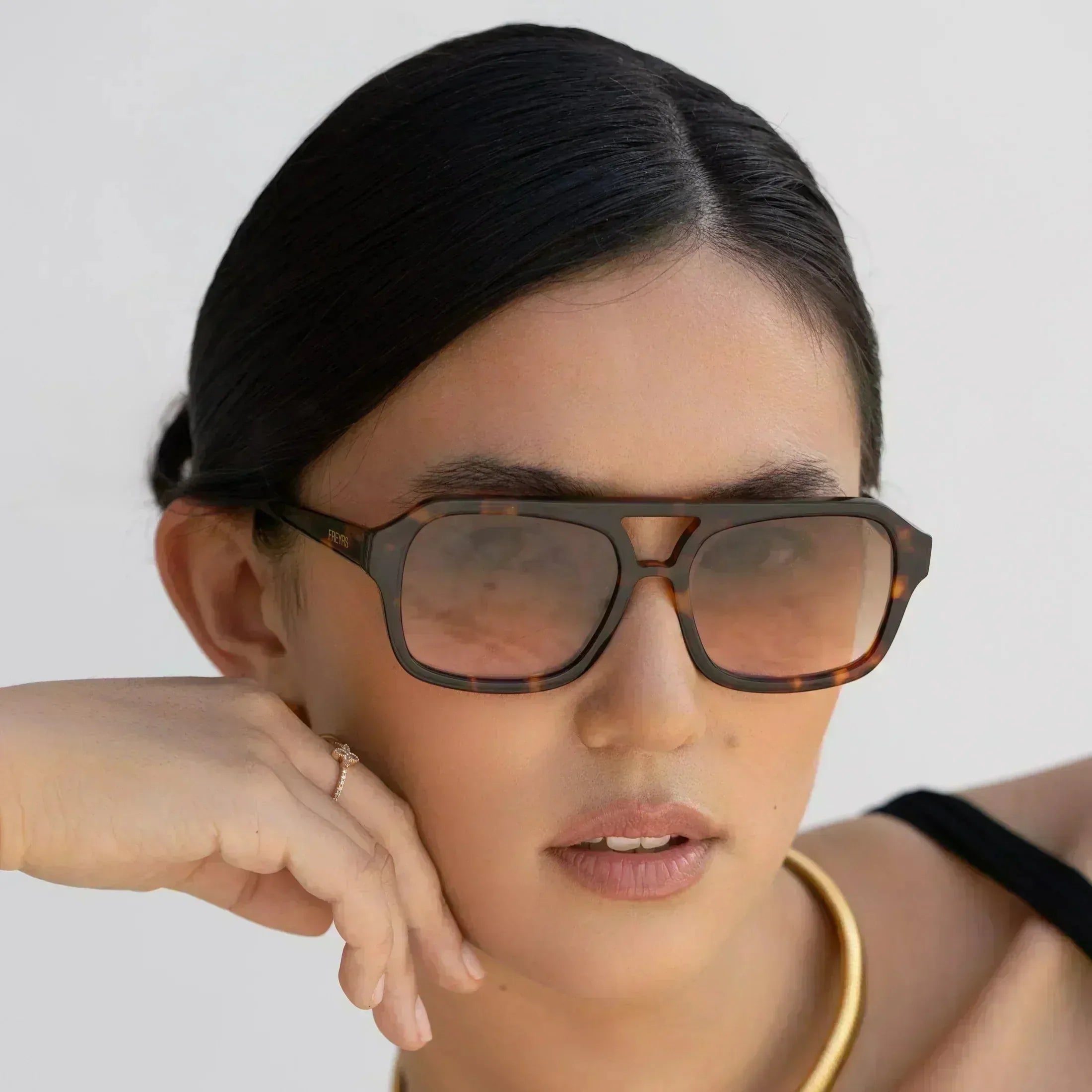 Havana luxury aviator sunglasses with tortoiseshell frames and gradient lenses worn by a woman with her hand resting on her