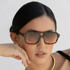 Havana luxury aviator sunglasses with tortoiseshell frames and gradient lenses worn by a woman with her hand resting on her