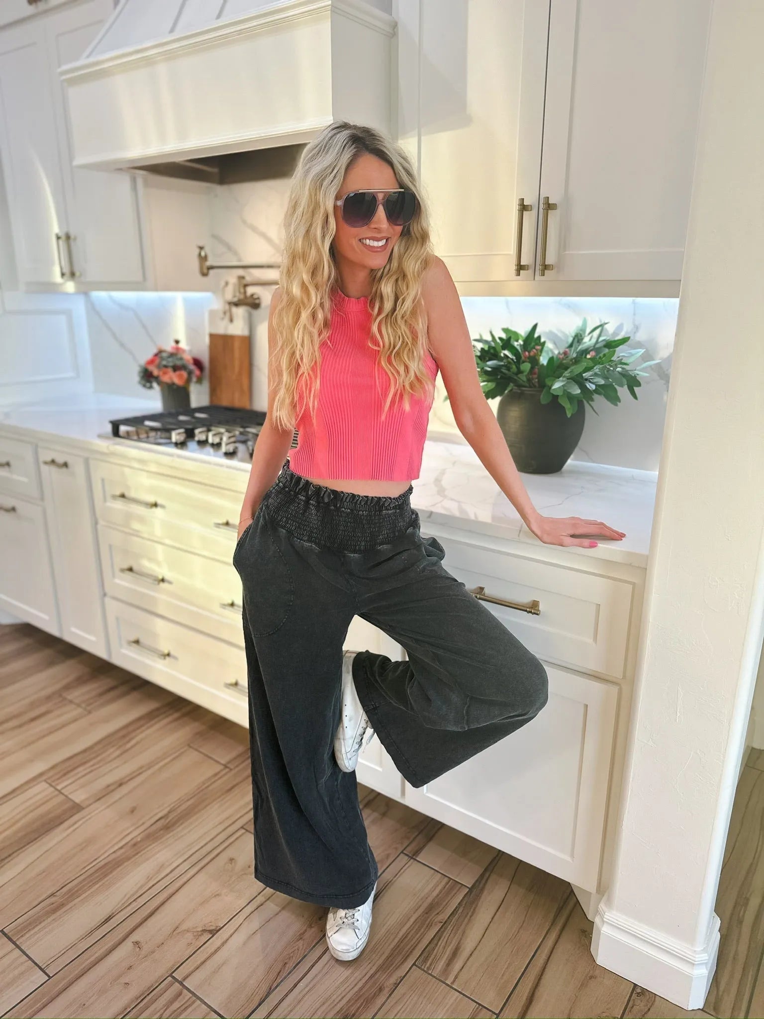Woman wearing HyFVE black wash elastic waist wide-leg trousers and a pink crop top, leaning on a kitchen counter.