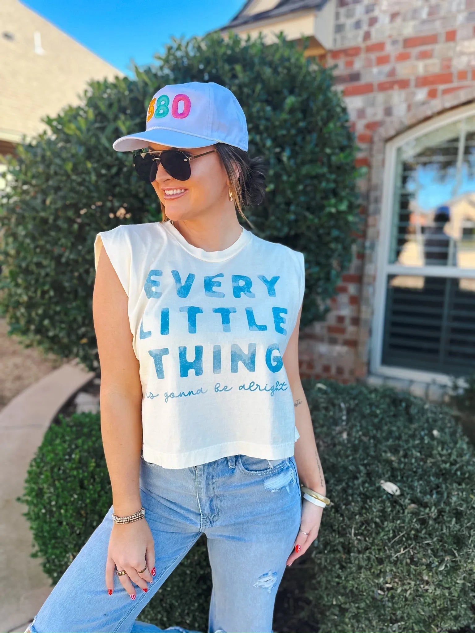 Woman wearing a white baseball cap with "580" embroidered on the front in colorful letters and a cream-colored sleeveless