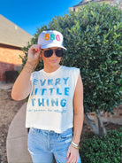 Woman wearing a white baseball cap with "580" embroidered in colorful letters and a white "Every Little Thing" graphic tee.