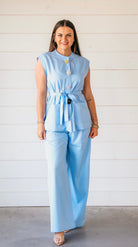 Light blue matching pant suit set with sleeveless belted top featuring decorative floral buttons and wide-leg pants.