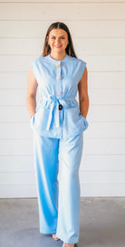 Light blue sleeveless pant suit with decorative floral buttons, tie waist, and wide-leg pants.
