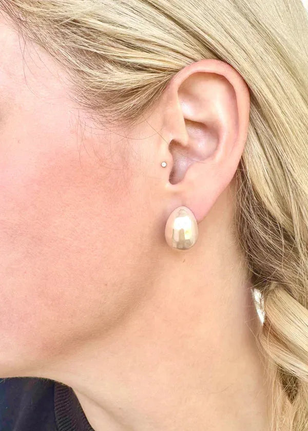 LINNY CO Surgical Steel Pearl Earrings: Droplet-shaped, polished, pearlized earrings dangle from a woman's earlobe.