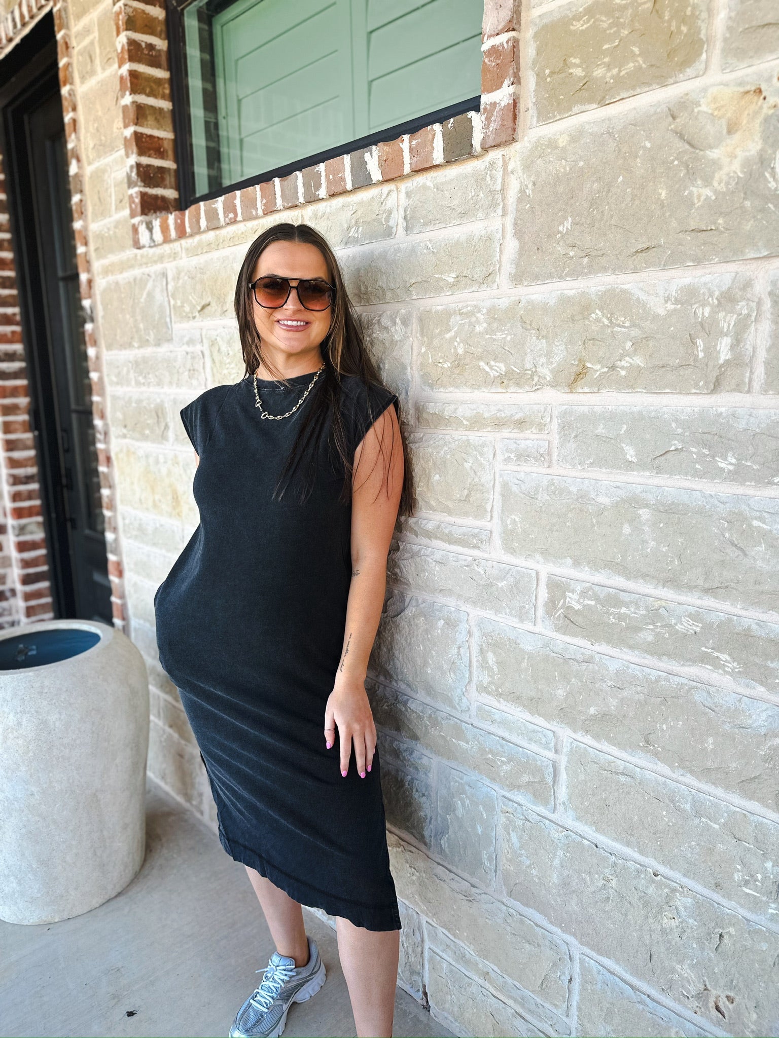 Model wearing a mineral wash oversized cotton midi dress in black with shoulder pads, sunglasses, silver necklace, and