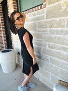 Woman in a black mineral wash oversized cotton midi dress with side slits, sunglasses, and sneakers.