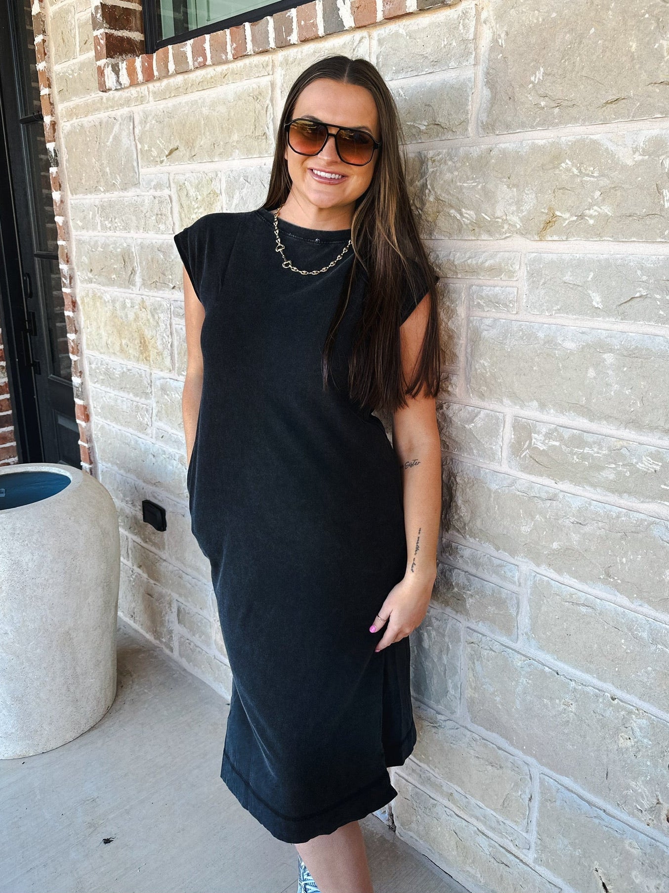 Woman wearing a mineral wash oversized cotton midi dress in black, with sunglasses and a gold chain necklace.