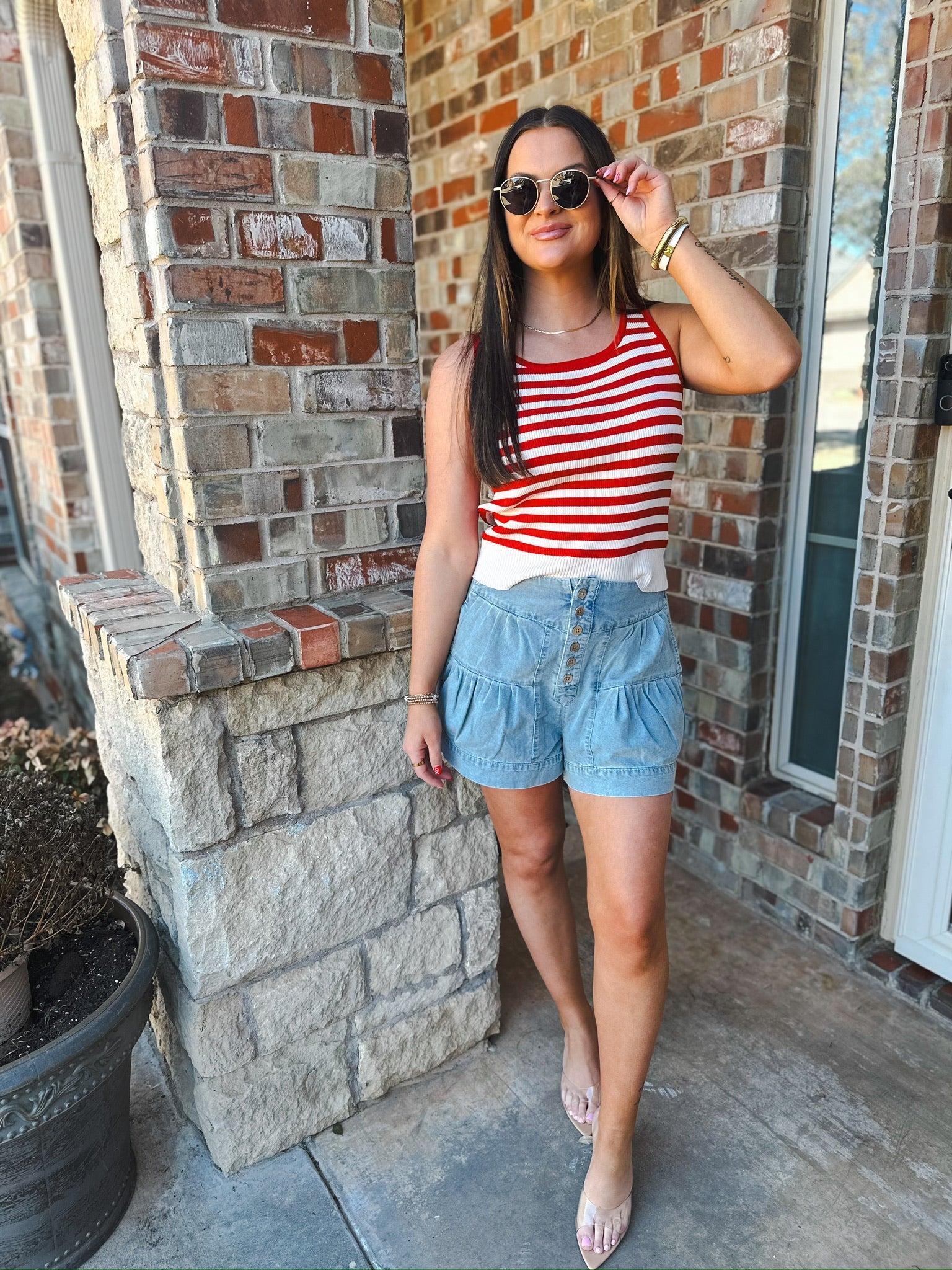 Model wearing mineral washed chambray high waist pleated shorts with button detail and a red and white striped tank top.