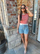 Model wearing mineral washed chambray high waist pleated shorts with button detail and a red and white striped tank top.