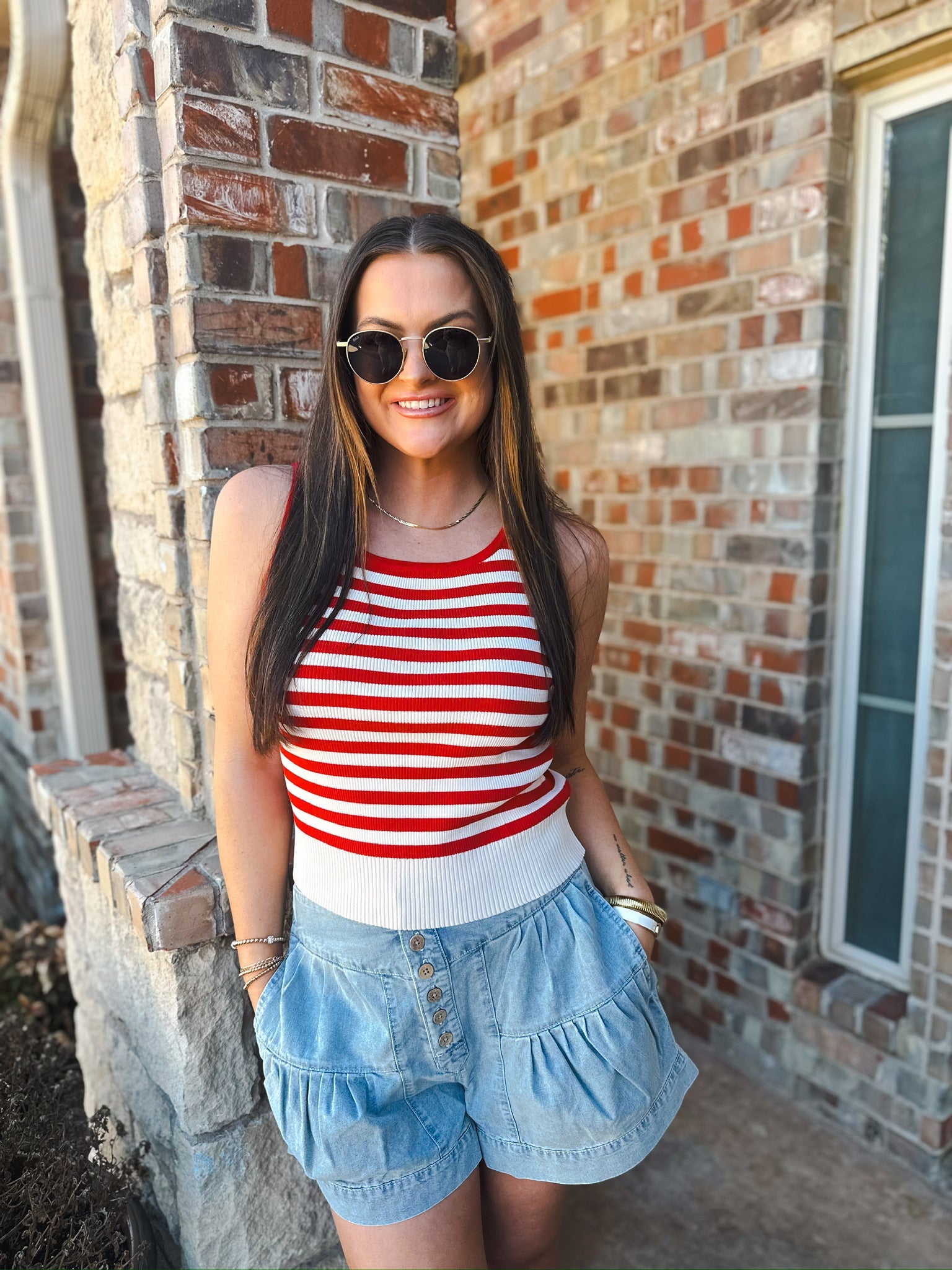Woman wearing red and white striped tank top and light blue chambray pleated shorts with button front.