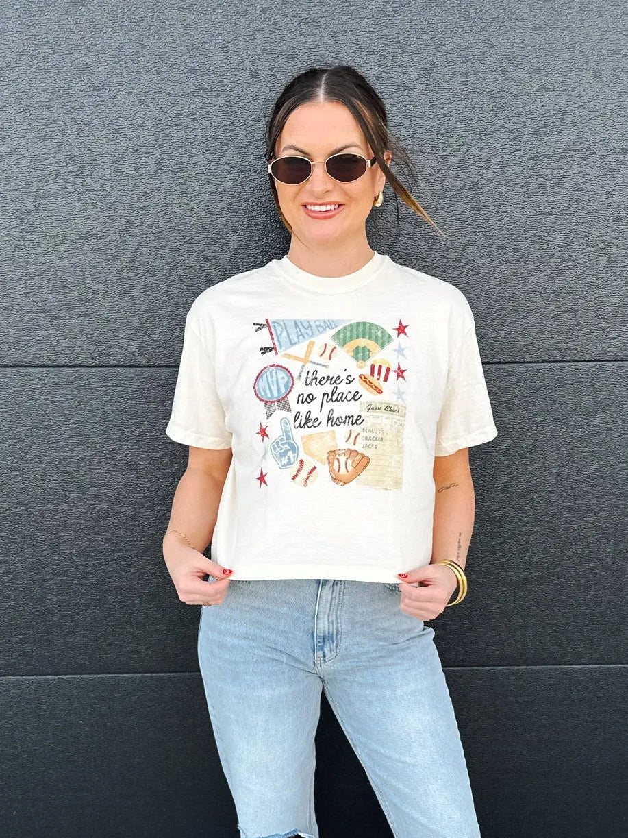 Cream graphic tee with "No Place Like Home" baseball design. Features baseballs, gloves, bats, and a fan finger.