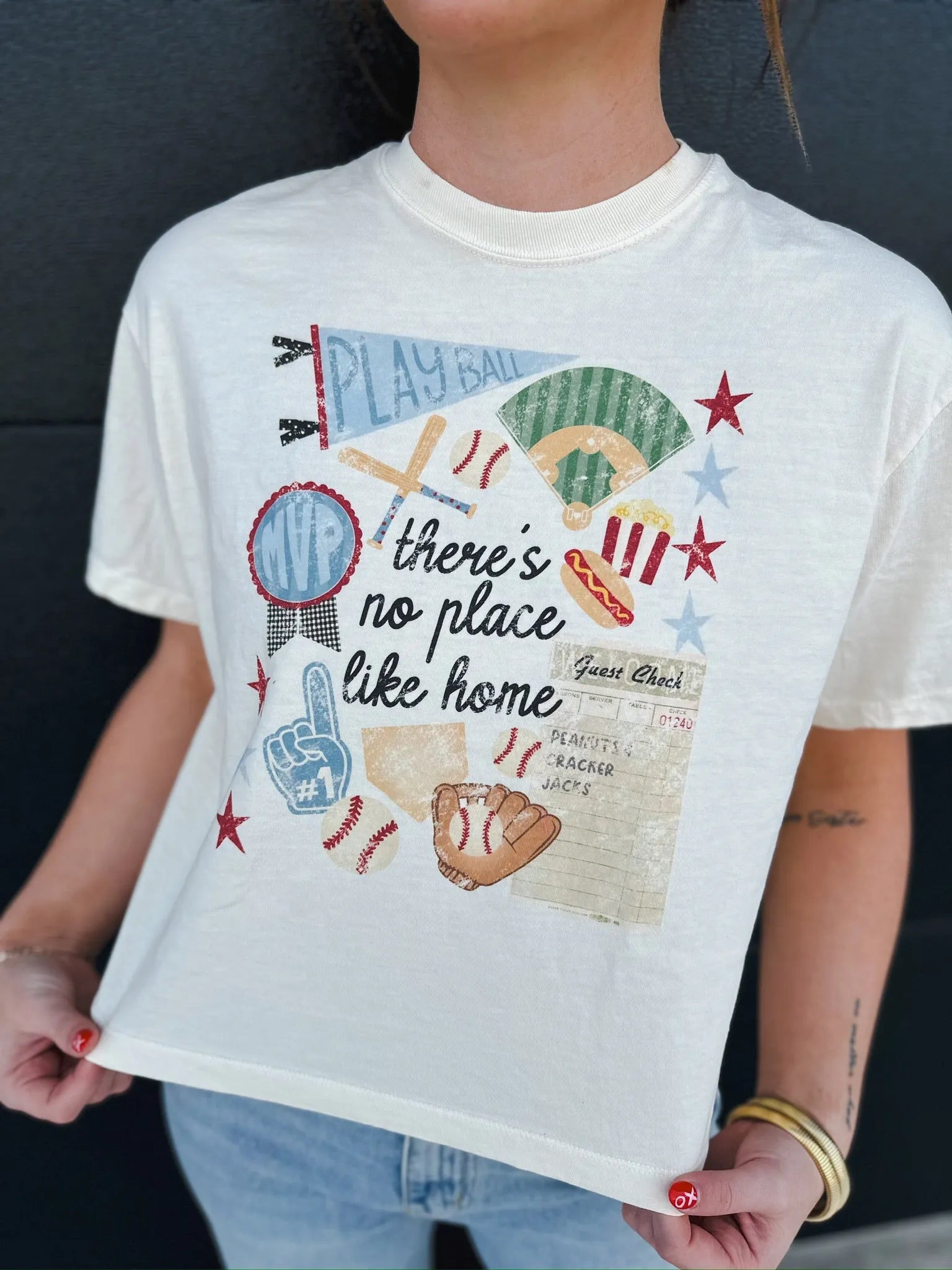 Cream graphic tee with baseball theme: 'Play Ball', baseball field, bats, gloves, hot dog, popcorn, MVP award, foam finger