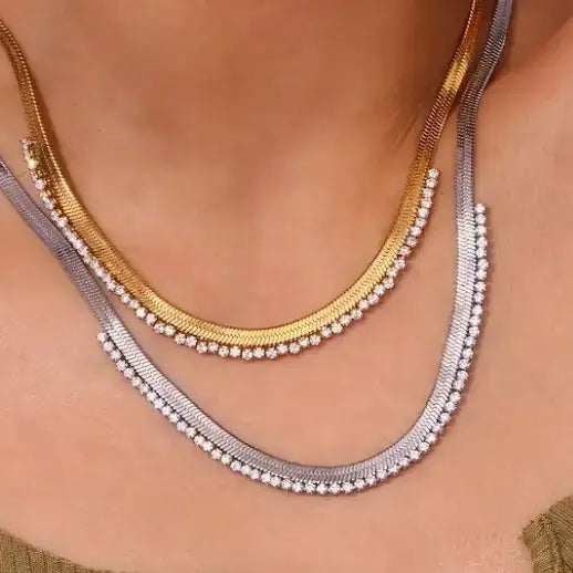 Two Noni crystal snake chain necklaces, one gold, one silver, layered on a neck.