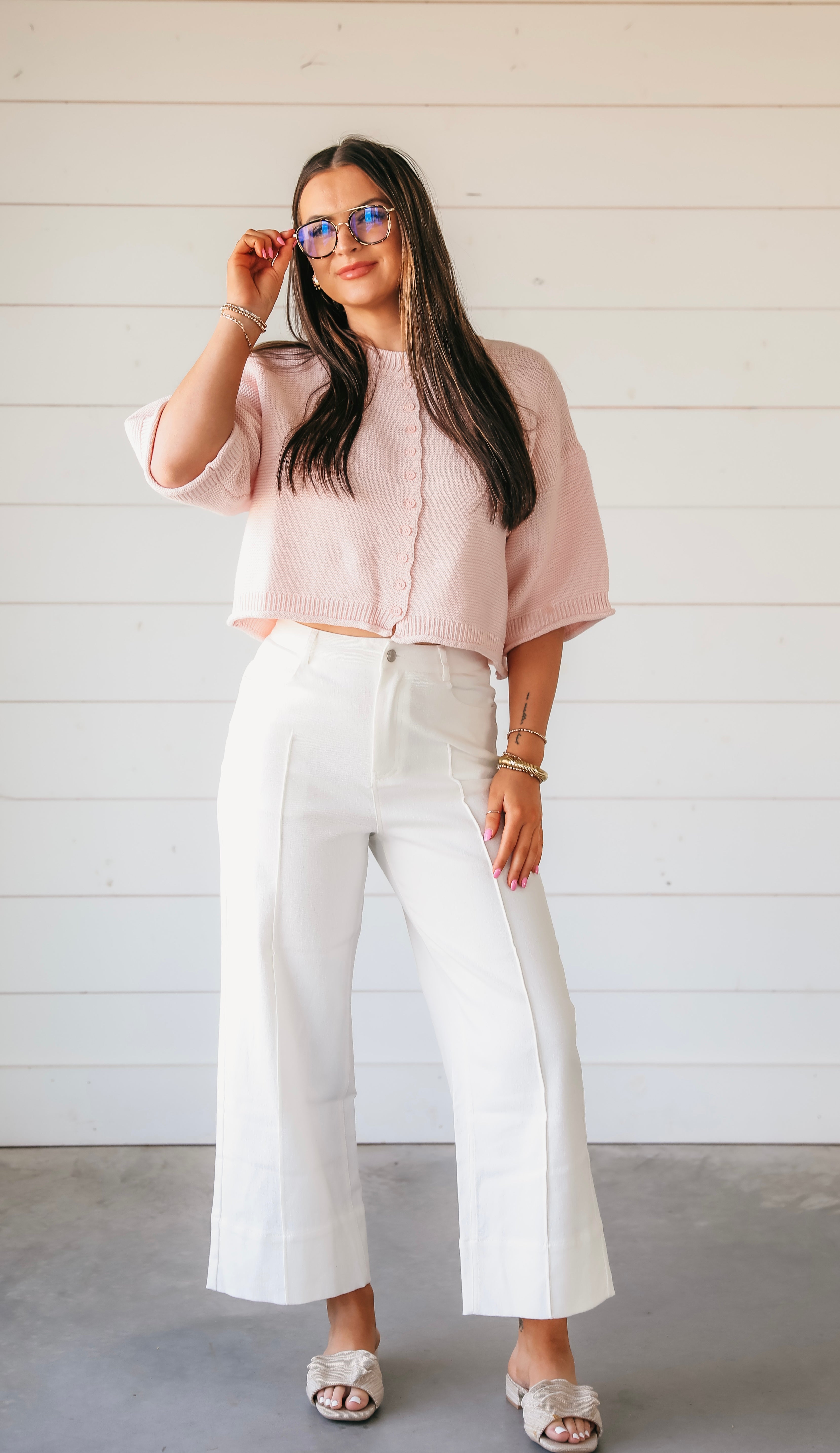 Woman wearing a pink waffle knit button-down cardigan with short sleeves and white wide-leg pants.