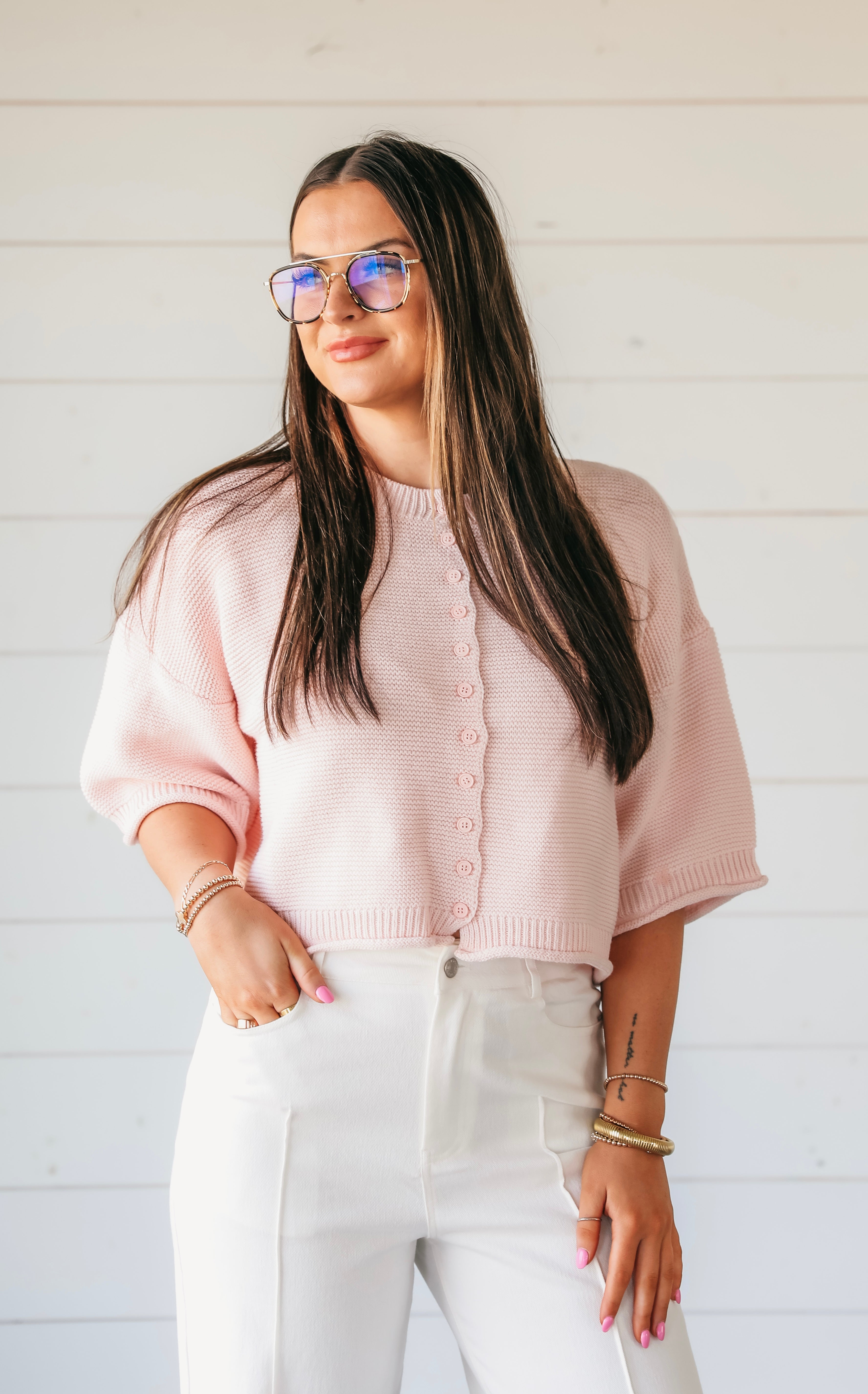 Woman wearing a light pink waffle knit button-down cardigan sweater with short sleeves and white pants. white pants.
