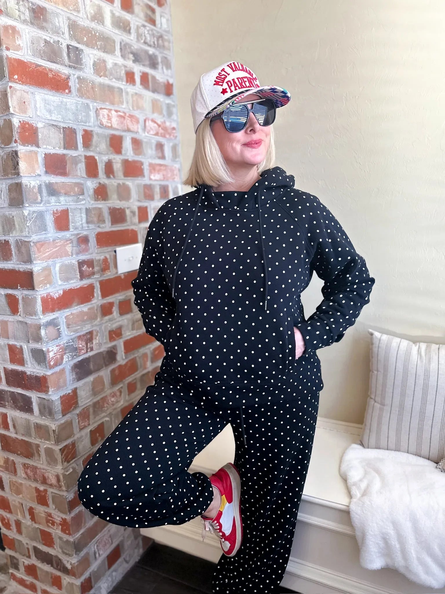 Poppy and Pine black and white polka dot sweatsuit. Woman wearing hoodie and pants with white polka dots. Red sneakers