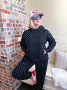 Poppy and Pine black and white polka dot sweatsuit. Woman wearing hoodie and pants with white polka dots. Red sneakers