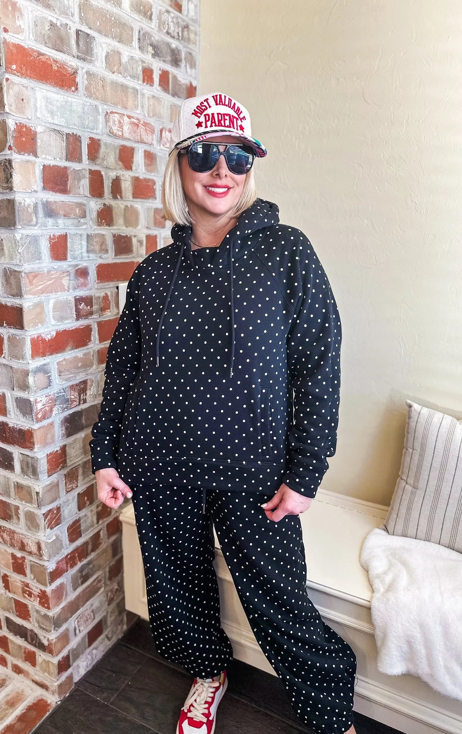 Woman wearing a black and white polka dot loungewear set, including a hooded sweatshirt and matching pants. She has blonde
