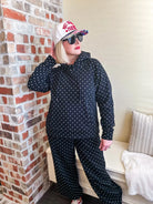 Black and white polka dot sweatsuit with drawstring hoodie and pants. Model wears a baseball cap and sunglasses.