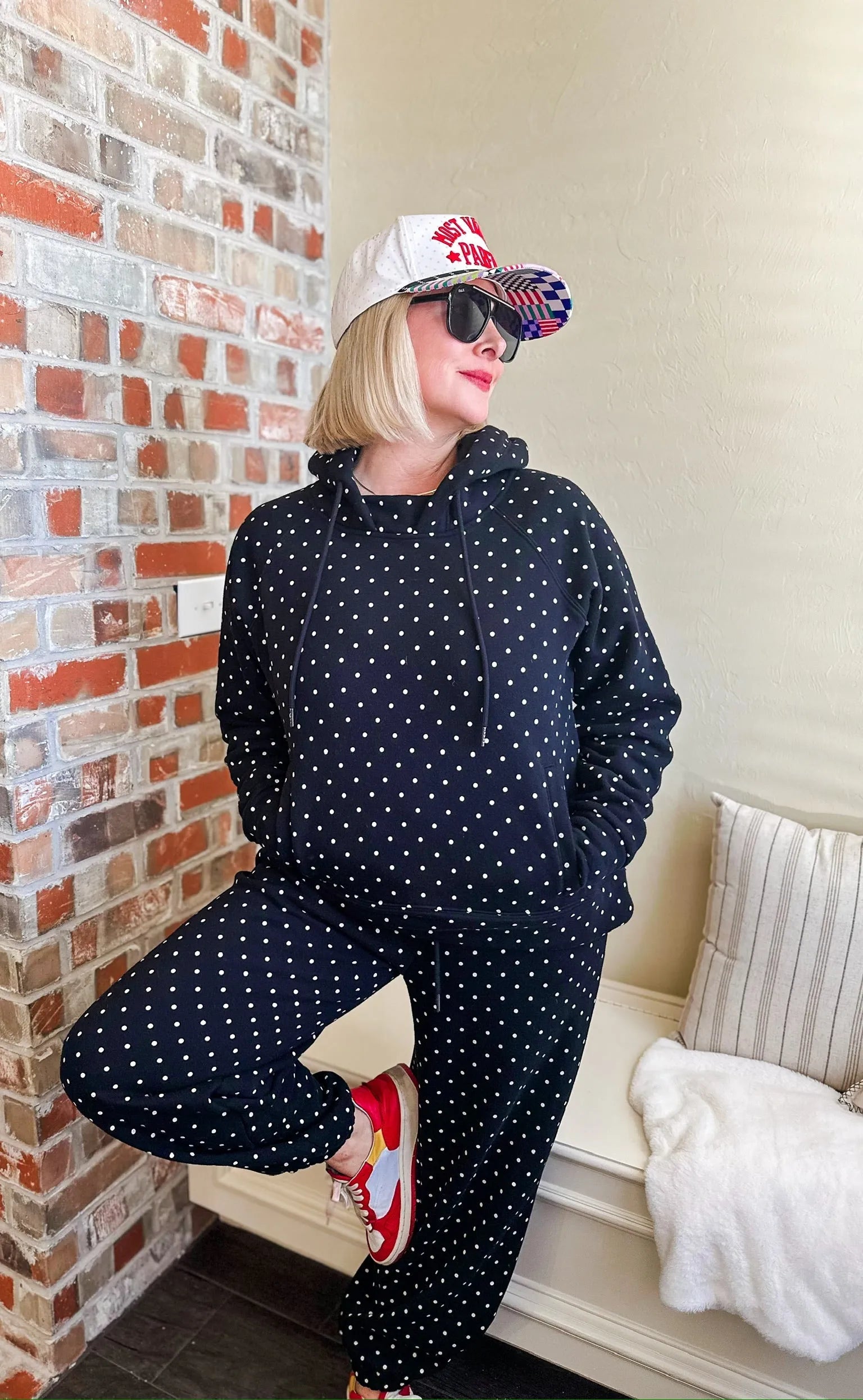 Black and white polka dot loungewear set including a hoodie and pants, worn by a woman with blonde hair and sunglasses.