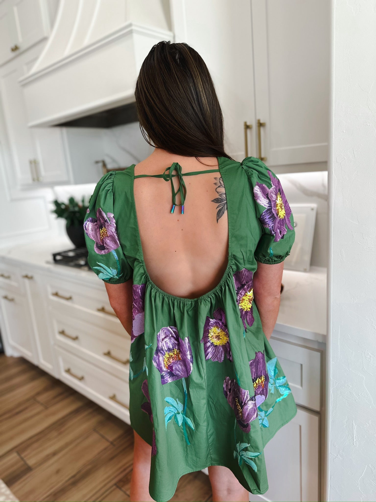 Green cotton dress with puff sleeves, featuring purple floral sequin embellishments. Open back with tie closure.