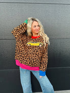 Queen of Sparkles leopard print sweater with yellow taxi cab graphic, red collar, pink hem, and blue cuffs.