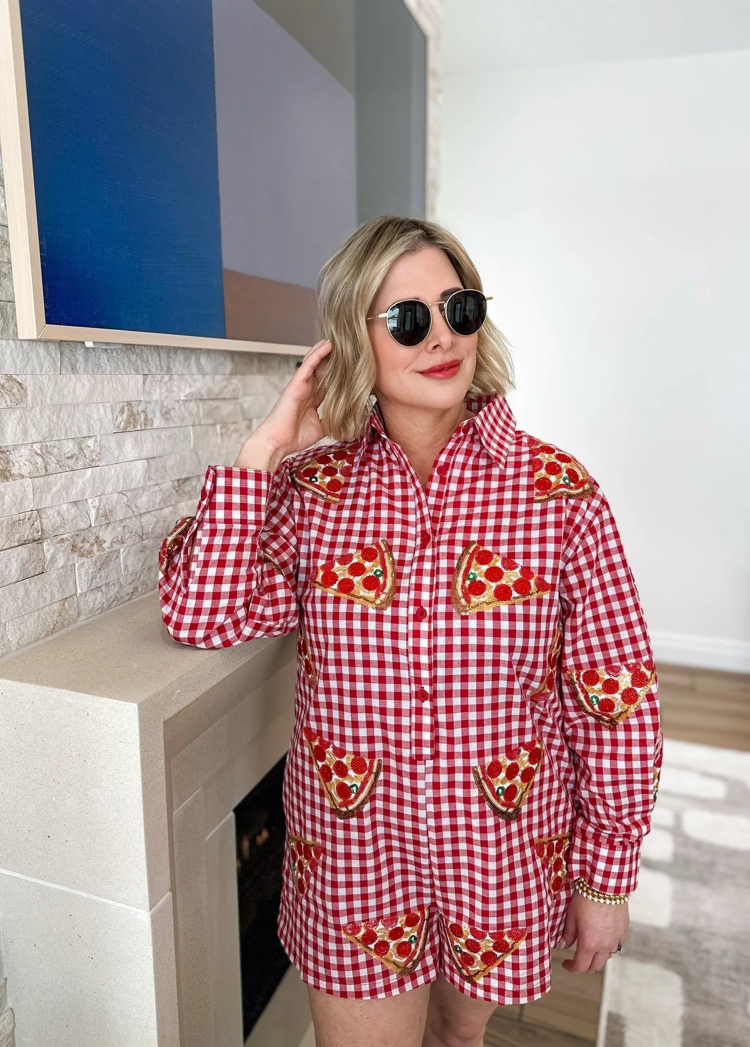 Red gingham romper with embroidered pizza slices, gold sequins, and red details. A woman wears the romper and sunglasses.