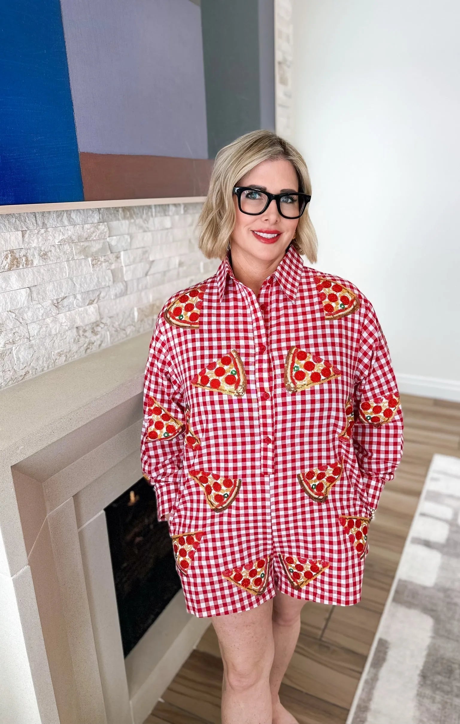 Queen of Sparkles red gingham romper adorned with sequined pizza slice patches. Woman wears glasses and red lipstick.