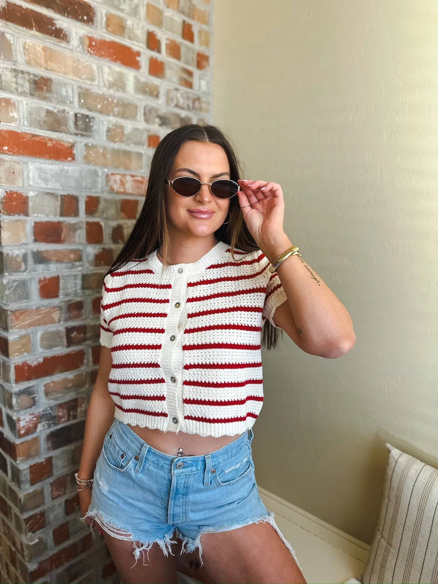 Woman wearing a red and cream striped short sleeve button-down cardigan sweater with crochet detail, paired with denim