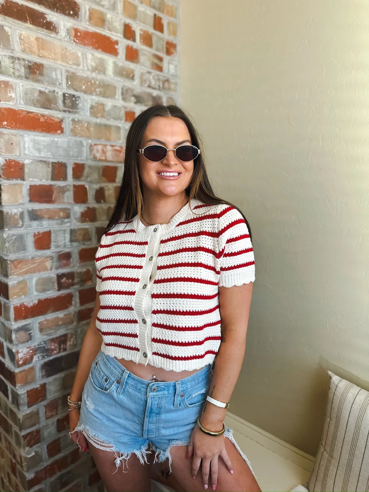 Cropped red and cream striped short sleeve button-down cardigan sweater with scalloped hem, worn by a woman with sunglasses