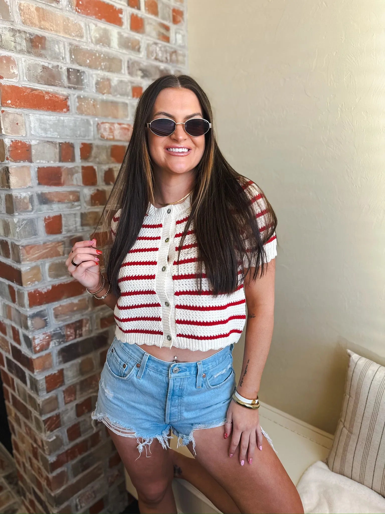 Woman wearing a red and cream striped short sleeve button down cardigan sweater with light wash distressed denim shorts and