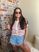 Woman wearing a red and cream striped short sleeve button down cardigan sweater with light wash distressed denim shorts and