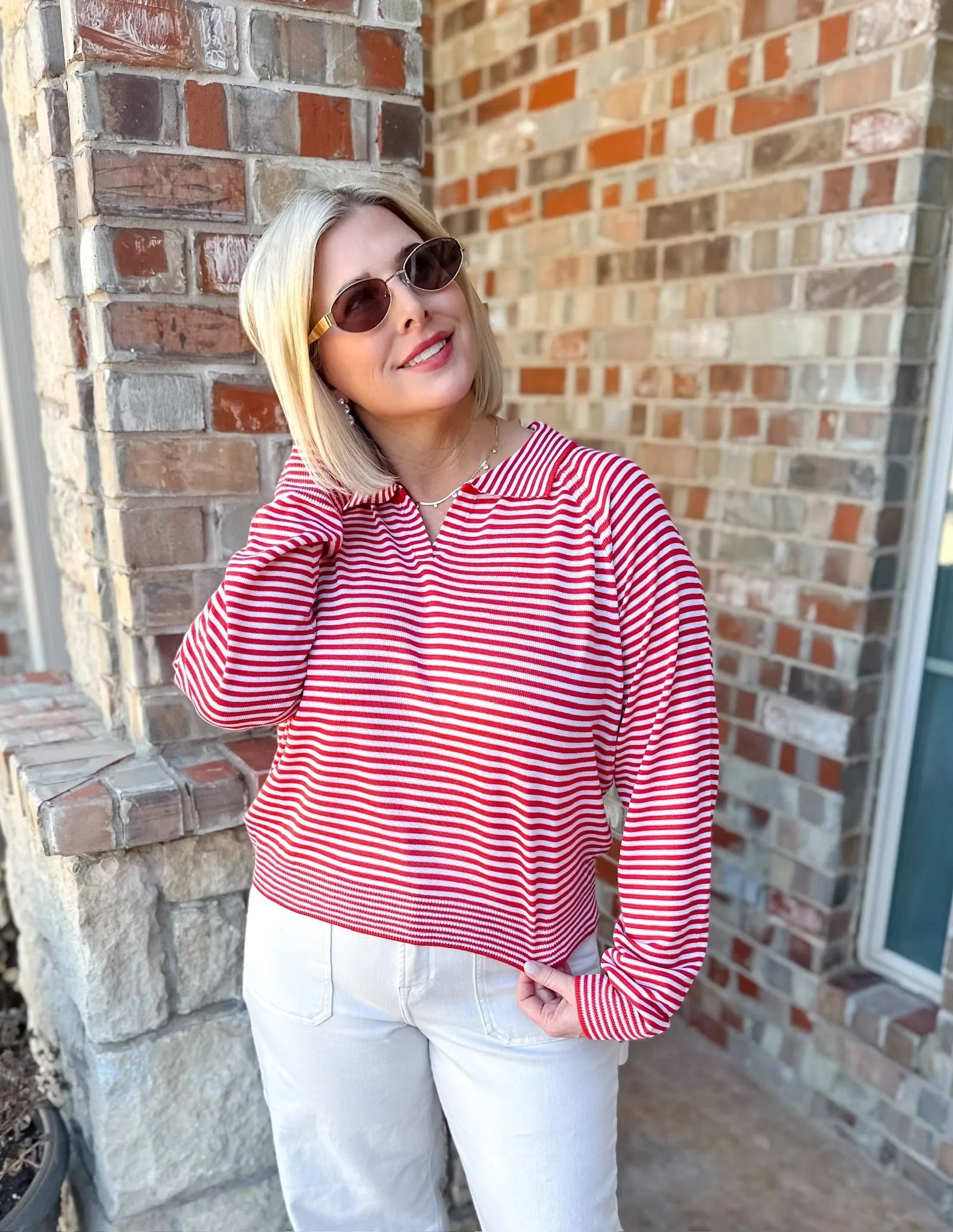 Woman wearing a red and cream striped long-sleeve collared sweater pullover top with white pants.