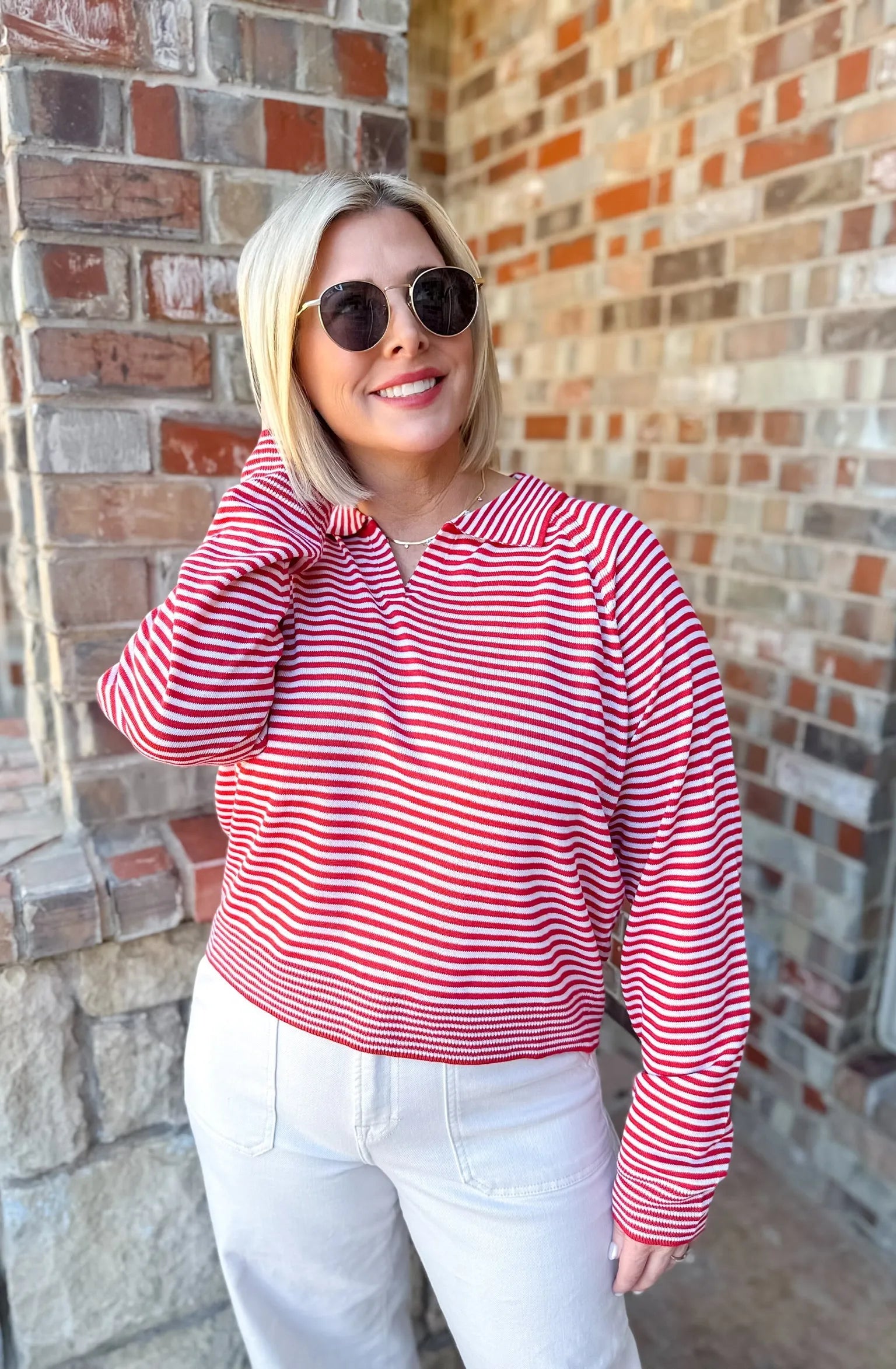 Woman wearing a red and cream horizontally striped collared knit sweater pullover top with white pants.