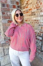 Woman wearing a red and cream horizontally striped collared knit sweater pullover top with white pants.