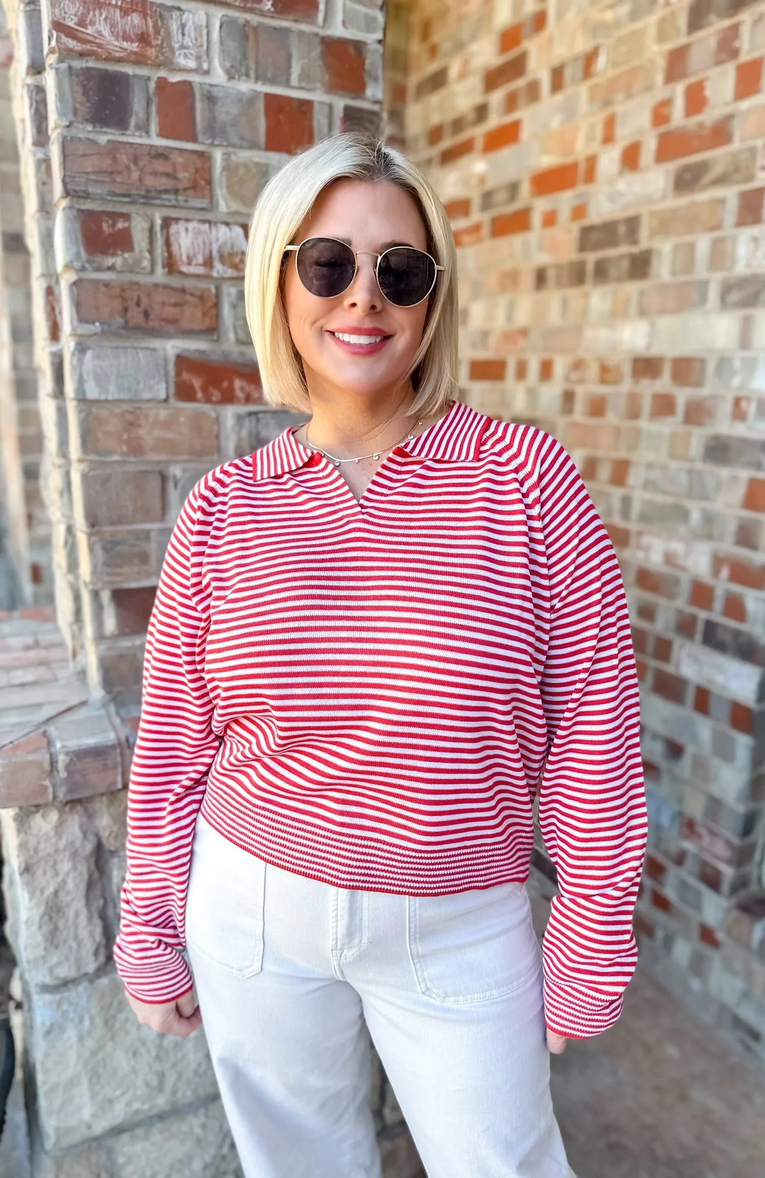Woman wearing a red and cream horizontal striped collared sweater pullover top and white pants.