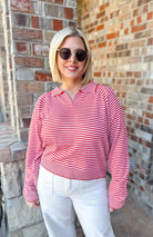 Woman wearing a red and cream horizontal striped collared sweater pullover top and white pants.