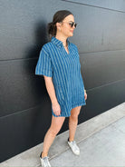 Woman wearing a relaxed fit, short sleeve, blue and white pinstripe denim split neck dress with two front pockets and white