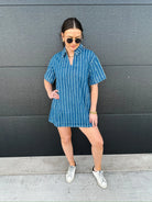 Woman wearing a short-sleeve denim dress with vertical white stripes and a split neckline, paired with white sneakers.