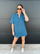 Woman wearing a relaxed fit short sleeve denim split neck dress with white vertical stripes. She has on sunglasses and