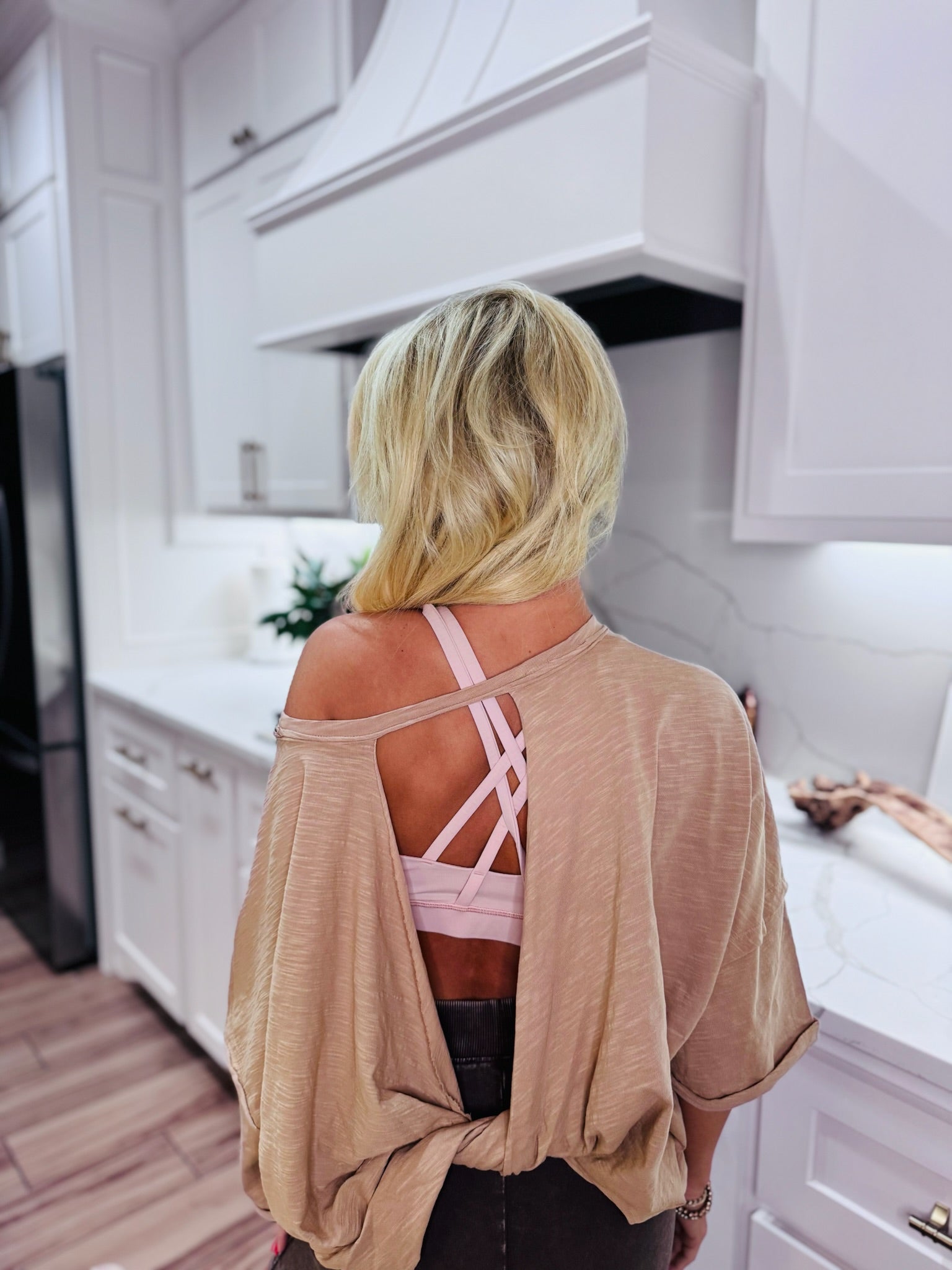Taupe twist back cropped tee showing pink strappy bra. Back view of woman in a taupe shirt with cutouts.
