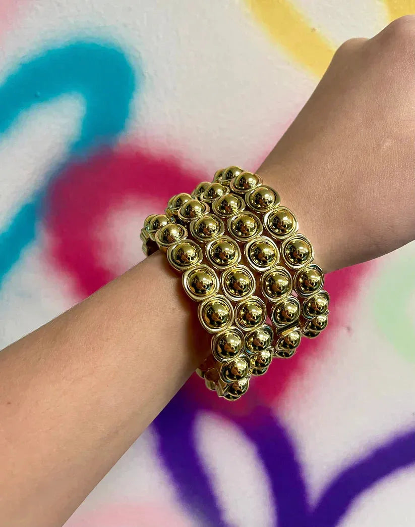 Taylor Shaye Pardi Gold Bracelet: A wide, multi-strand gold bracelet featuring rows of polished, spherical beads on a wrist.